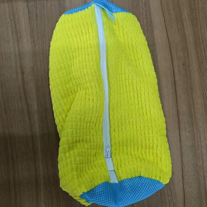 Upright yellow Shoe Washing Bag for Washing Machine with ribbed texture and blue base on wood
