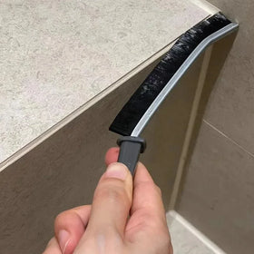 Hand holding a worn Grout & Tile Detail Brush Set brush against a tiled surface